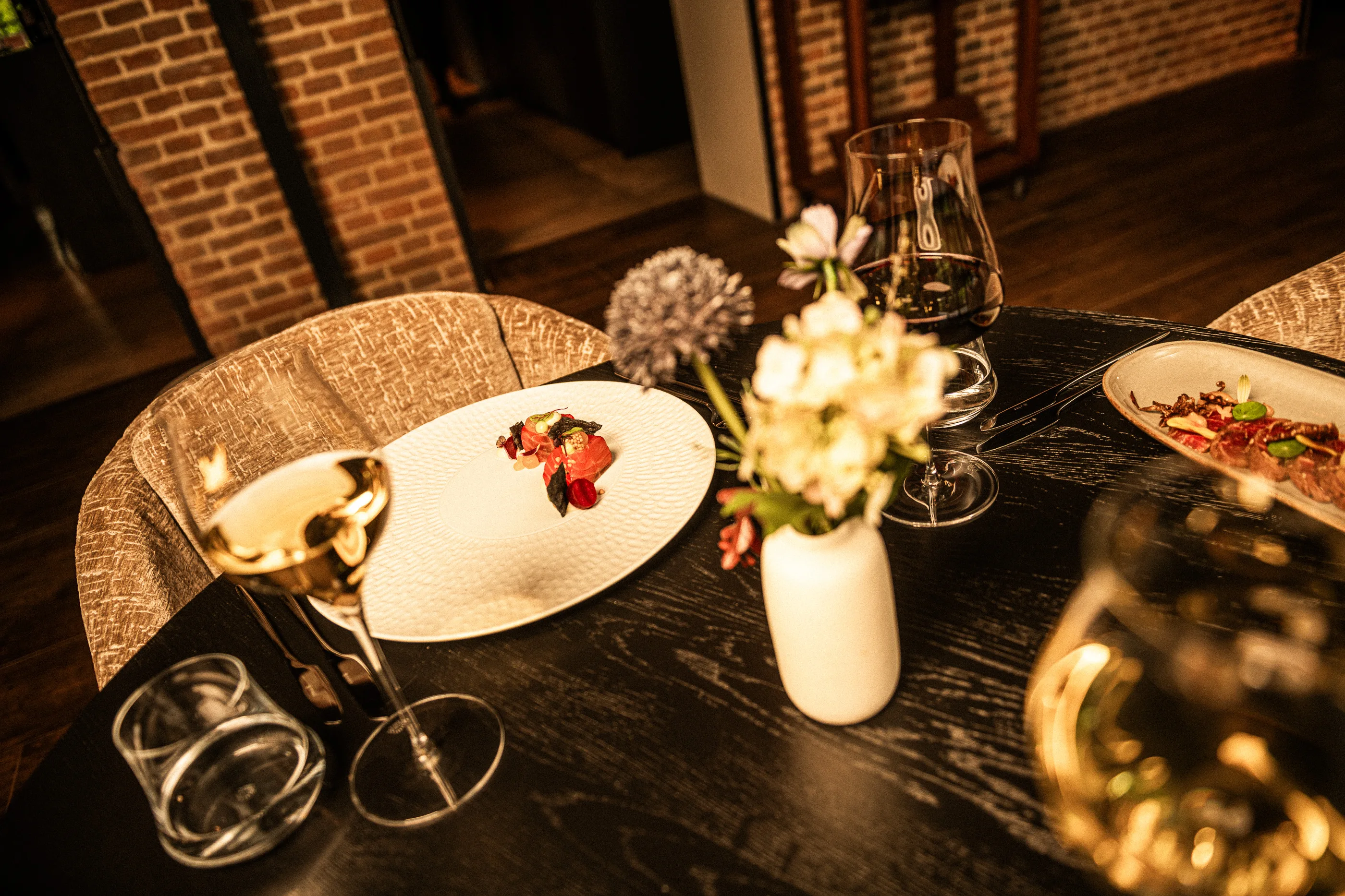 Een gedekte tafel met een voorgerecht, bloemen en wijn in restaurant De Kastanjefabriek